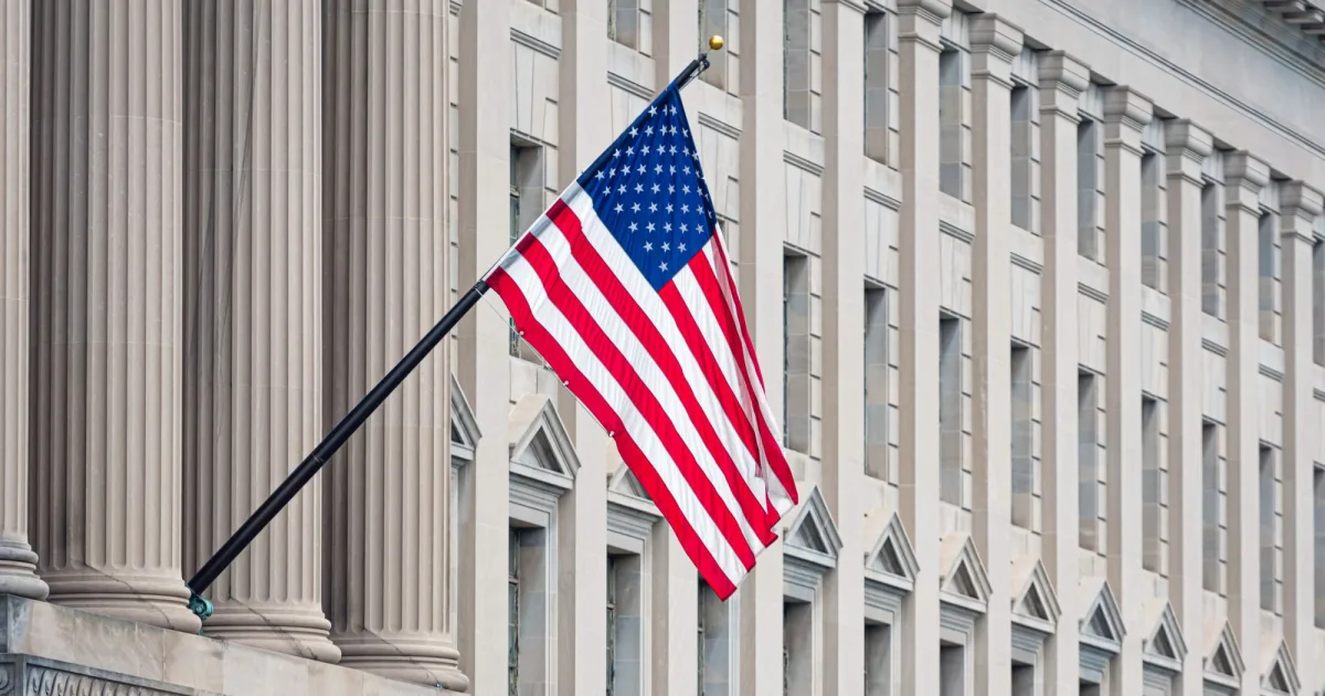 政府庁舎の柱に掲げられたアメリカ国旗。米財務省が長期国債の買い戻し枠を倍増した件を解説する記事のヘッダー画像