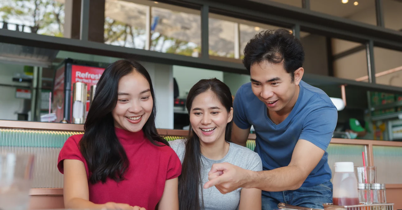 明るいレストランでメニューを一緒にのぞき込み、笑顔で料理を選ぶ3人の客