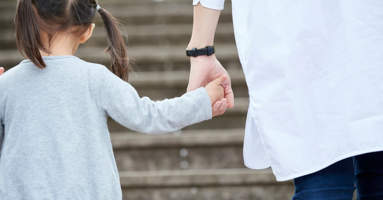 石段の前で、小さな女の子が大人と手をつないで歩いている後ろ姿